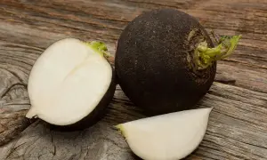 Cała i przekrojona czarna rzepa na drewnianym blacie. W środku biały, soczysty miąższ.