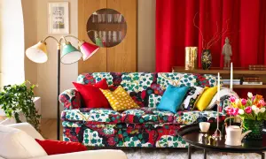 Sofá con estampado floral vibrante, cojines coloridos y una lámpara de pie que evoca un estilo vintage.