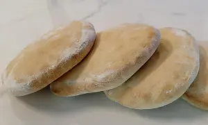 Quatre pains arabes dorés, légèrement saupoudrés de farine, prêts à être garnir.