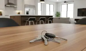 Clés sur une table en bois, symbolisant la vente d'un appartement loué. Cuisine moderne et salon en arrière-plan.