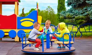 Trzech chłopców bawi się na karuzeli na kolorowym placu zabaw.
