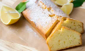 Saftiger veganer Zitronenkuchen, bestäubt mit Puderzucker, mit frischen Zitronenspalten und Blättern dekoriert.