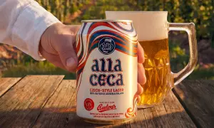 Mano che tiene una lattina di Budweiser ceca "Alla Ceca", con una birra in un boccale sullo sfondo.