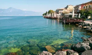 Lungolago di Gardone Riviera: cosa vedere? Case colorate, ristoranti con tavoli all'aperto e il lago cristallino.