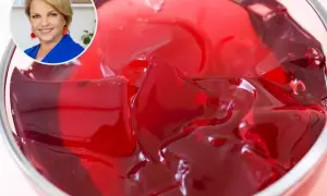 Czerwona galaretka w pucharku, obok uśmiechnięta kobieta. Dowiedz się, ile czasu tężeje galaretka w zamrażarce.