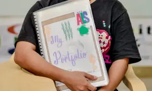 Ein Kind hält ein bunt gestaltetes Portfolio für den Kindergarten mit Seepferdchen und Schildkröten.
