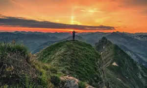 Sonnenuntergang auf der Kanisfluh Wanderung. Ein Wanderer steht mit ausgebreiteten Armen auf dem Gipfel und genießt den atemberaubenden Ausblick.