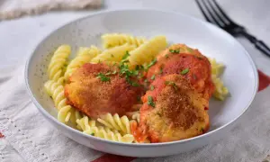 Kotlety w sosie pomidorowym z makaronem fusilli, posypane natką pietruszki.