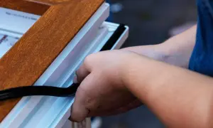 Pose d'un joint d'étanchéité pour comment insonoriser une porte. Les mains insèrent un joint noir dans le cadre blanc d'une porte imitation bois.