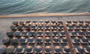 Rzędy leżaków pod słomianymi parasolami na plaży w Sithonii, z morzem w tle.