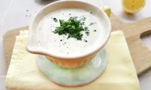 Cremige Schüssel mit frischem Ranch Dressing, garniert mit Petersilie und Pfeffer. Daneben liegen Zitronenspalten und ein Stapel Servietten.