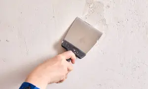 Mano con espátula realizando el alisado de paredes, preparando la superficie para un acabado perfecto.