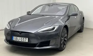 En mörkgrå Tesla Model S, en begagnad elbil med svensk registreringsskylt UBJ 037, står parkerad inomhus.
