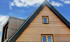 Moderne holzfassade mit horizontalen Holzlamellen und Fenstern unter blauem Himmel mit Wolken.
