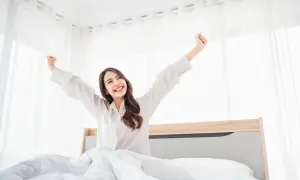 A woman stretches happily in bed, a perfect example of how to wake up with more energy.