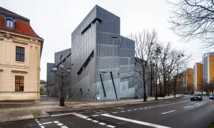 Nowoczesny budynek muzeum żydowskiego w Berlinie, obok starszej kamienicy, z charakterystyczną, poszarpaną fasadą.