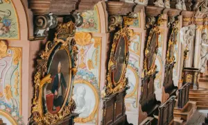Wnętrze z portretami w złotych ramach, ozdobnymi malowidłami i rzeźbami. Idealizm epoki widoczny w kunsztownych detalach.