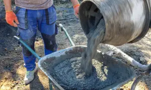 Betoniarka wylewa beton do taczki, pracownik w rękawicach stoi obok.
