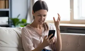 Femme frustrée sur son canapé, regardant son téléphone avec exaspération. Elle dit : "Je ne capte pas chez moi !