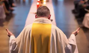 Kapłan w białej szacie z żółtym pasem, z rękami uniesionymi w geście modlitwy, zastanawia się, czy praca w niedziele i święta jest zawsze grzechem. Dylemat zawodowy.