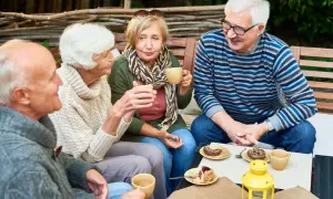 Czterech seniorów przy kawie i ciastkach. Choć wydaje się, że nie ma mowy o samotności na emeryturze, ich spojrzenia sugerują coś innego.