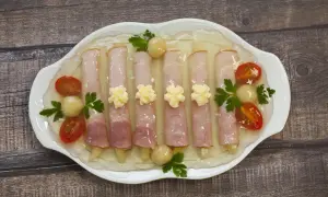 Szparagi w szynce w galarecie, ozdobione pomidorkami koktajlowymi i majonezem, prezentują się apetycznie na białej paterze.