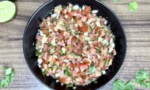 Świeże, kolorowe pico de gallo w czarnej misce, z limonkami i kolendrą na drewnianym tle. Idealne do nachos!