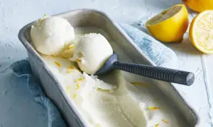 En metallform fylld med krämig italiensk citronsorbet, garnerad med citronskal. Två skopor är upptagna med en skopa.