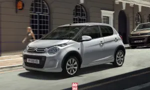 Srebrny Citroën C1 z czarnymi nakładkami na błotniki przemierza miejską ulicę.