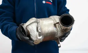 Osoba w rękawiczkach trzyma metalowy element, prawdopodobnie **fap** (filtr cząstek stałych) do samochodu.
