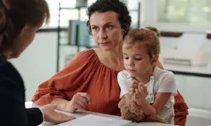 Matka z córką słuchają diagnozy autyzmu. Dziecko tuli misia, a kobieta patrzy z uwagą.