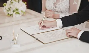 Pan młody podpisuje dokumenty ślubne, obok bukiet ślubny.