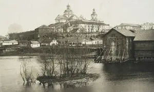 Widok na miasto z rzeką i kościołem w tle. Drewniane budynki nad wodą, mała wysepka z drzewami. Pisz na Berdyczów!