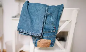 Złożone, klasyczne jeansy Levi Strauss wiszą na białym krześle. Widoczna metka z logo marki.