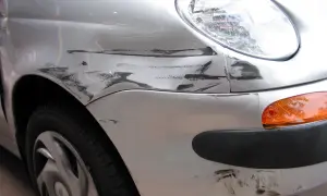 Uszkodzony srebrny błotnik i zderzak auta z widocznymi śladami po otarciu. Jak usunąć rysy z auta?