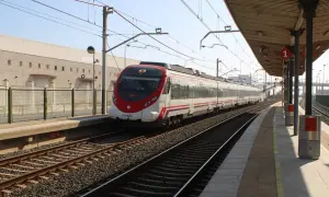 Nowoczesny pociąg Renfe z czerwonym przodem stoi na stacji. W tle budynek i peron.