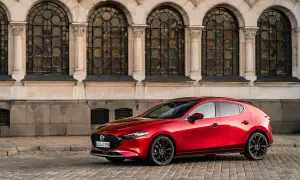 Un elegante Mazda 3 Skyactiv X rojo, con sus líneas fluidas, se detiene frente a una fachada histórica con arcos y vidrieras.