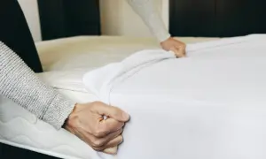 Hands pulling a white mattress pad over a mattress. This is part of how to clean a mattress pad.