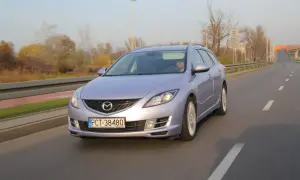 Jasny Mazda 6 kombi jedzie po drodze, jej żarówki mijania oświetlają trasę.