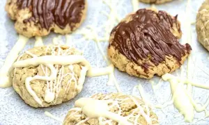 Leckere Haferflocken Kekse, einige mit Schokoladenglasur, andere mit weißer Schokolade verziert, auf einem hellen Untergrund.