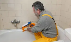 Mann erneuert mit Kartuschenpresse die silikonfugen an der Badewanne.