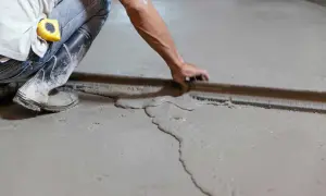 Obrero usa regla para nivelar suelo de cemento fresco.