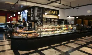 En kvinna arbetar bakom disken på Fazer Café i Helsingfors. Disken är fylld med bakverk och tårtor.
