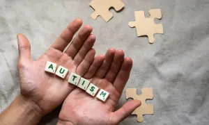 Twee handen houden de letters vast die 'AUTISME' spellen. Puzzelstukjes liggen verspreid, symbolisch voor het spectrum.