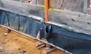 Baustelle mit Noppenbahn und Sand. Eine Horizontalsperre aus Bitumenbahn schützt die Wand vor Feuchtigkeit.