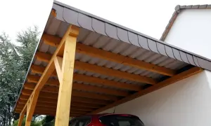 Drewniana wiata z szarym dachem, gotowa do ochrony czerwonego samochodu.