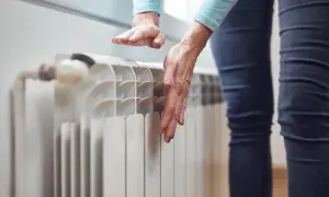 Ręce sprawdzają temperaturę grzejnika, zastanawiając się, dlaczego grzejnik jest zimny na dole.