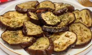 Rodajas de berenjenas asadas al horno, tiernas y doradas, espolvoreadas con hierbas aromáticas.
