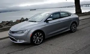 Srebrny Chrysler 200s zaparkowany nad wodą, z palmą i mostem w tle.