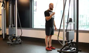 Mężczyzna wykonuje prostowanie ramion na wyciągu, ćwicząc triceps.
